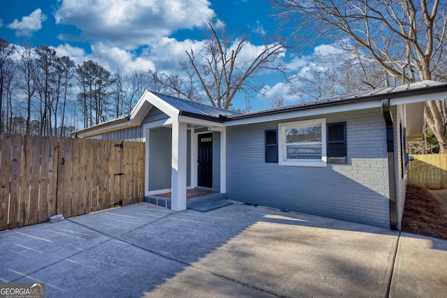 exterior space with a patio area, fence, brick siding, and metal roof