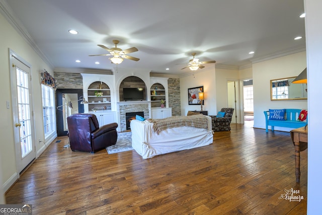 living room featuring built in shelves, dark wood-type flooring, ornamental molding, and ceiling fan