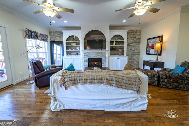 living room with a stone fireplace, ornamental molding, dark hardwood / wood-style floors, and ceiling fan