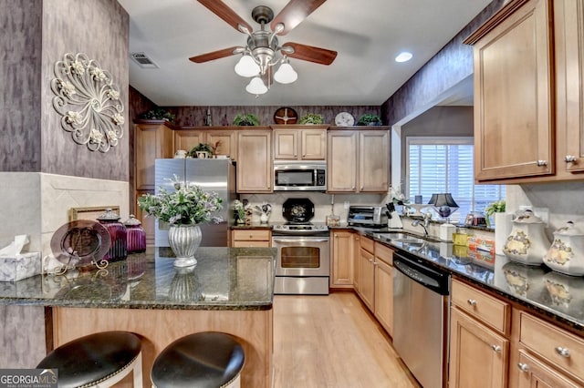 kitchen featuring appliances with stainless steel finishes, dark stone counters, sink, ceiling fan, and a breakfast bar