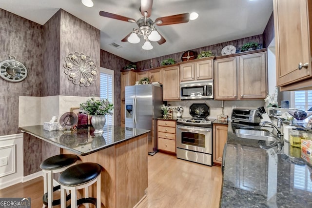 kitchen with appliances with stainless steel finishes, dark stone countertops, a kitchen breakfast bar, sink, and light wood-type flooring