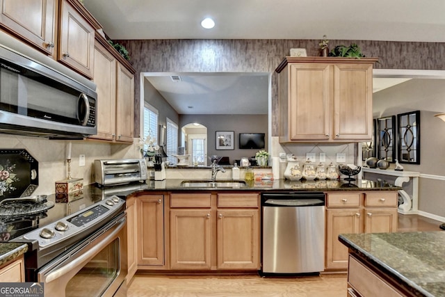 kitchen featuring stainless steel appliances, dark stone counters, sink, kitchen peninsula, and light wood-type flooring