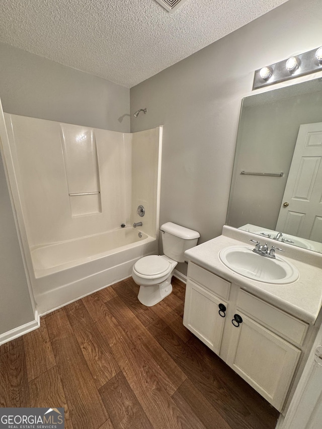 full bathroom featuring toilet, a textured ceiling, wood-type flooring, vanity, and washtub / shower combination