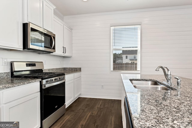 kitchen with stone counters, wooden walls, sink, white cabinets, and stainless steel appliances