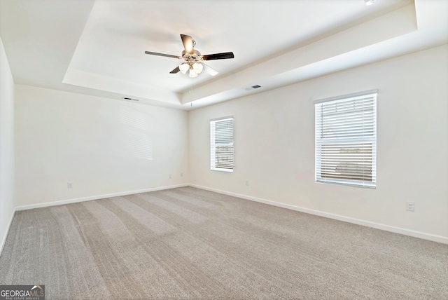 unfurnished room with light colored carpet, ceiling fan, and a raised ceiling