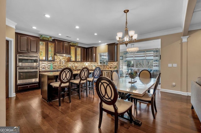 dining room featuring crown molding, dark hardwood / wood-style flooring, a chandelier, and decorative columns