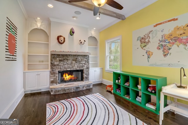 game room with crown molding, built in features, dark hardwood / wood-style floors, and a stone fireplace