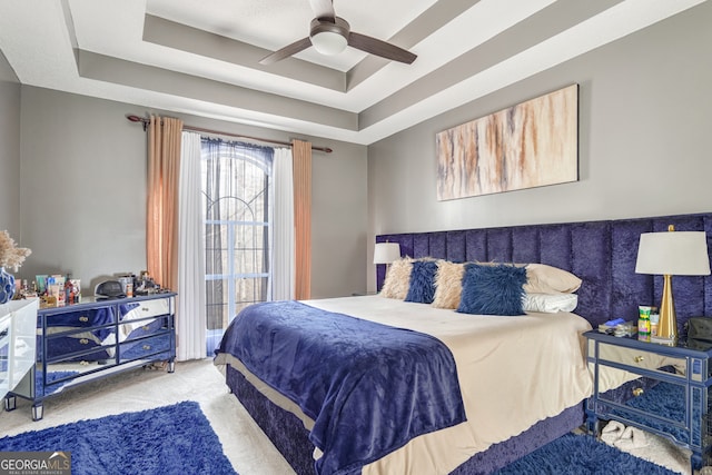 carpeted bedroom featuring ceiling fan and a tray ceiling