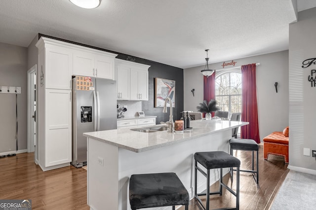 kitchen featuring sink, white cabinets, a kitchen breakfast bar, stainless steel fridge with ice dispenser, and a center island with sink