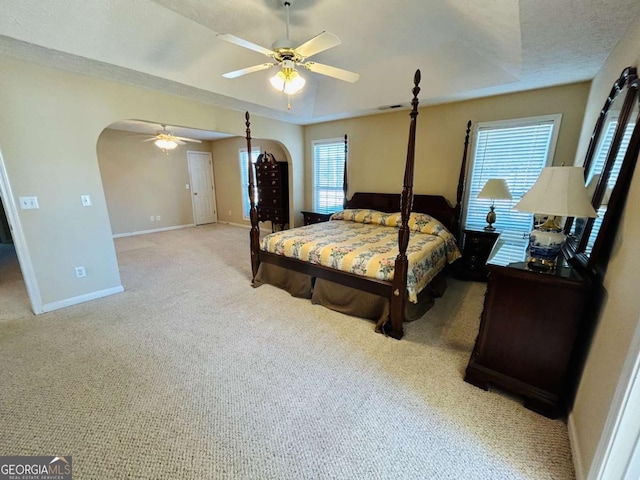 bedroom with ceiling fan, light colored carpet, a textured ceiling, and a tray ceiling