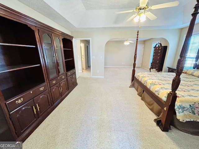 bedroom with ceiling fan, light colored carpet, a textured ceiling, and a tray ceiling