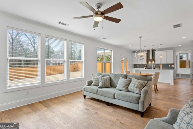 living room with light wood-type flooring, ceiling fan with notable chandelier, a healthy amount of sunlight, and ornamental molding