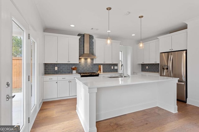 kitchen with white cabinetry, wall chimney range hood, sink, a center island with sink, and stainless steel fridge