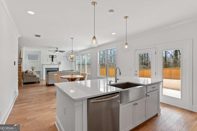 kitchen with stainless steel dishwasher, sink, white cabinetry, a kitchen island with sink, and ornamental molding