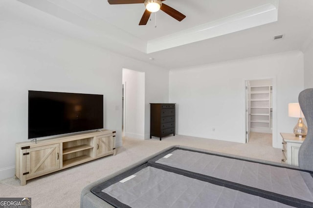 carpeted bedroom featuring a spacious closet, crown molding, a closet, ceiling fan, and a tray ceiling