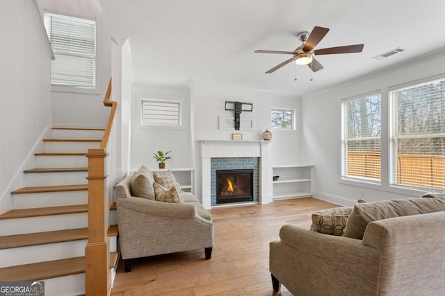 living room featuring ceiling fan, light hardwood / wood-style flooring, crown molding, and a fireplace