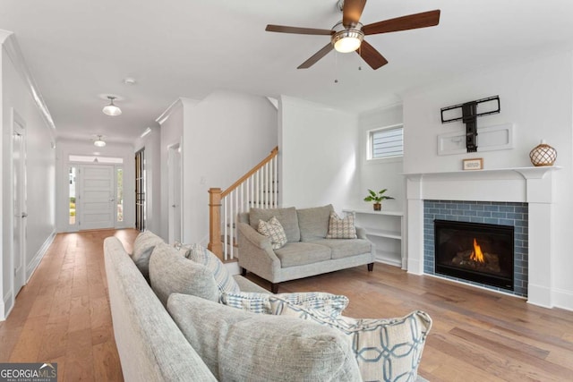 living room with light hardwood / wood-style floors, a tile fireplace, ornamental molding, and ceiling fan