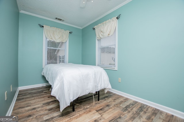 bedroom featuring ceiling fan, a textured ceiling, hardwood / wood-style flooring, and ornamental molding