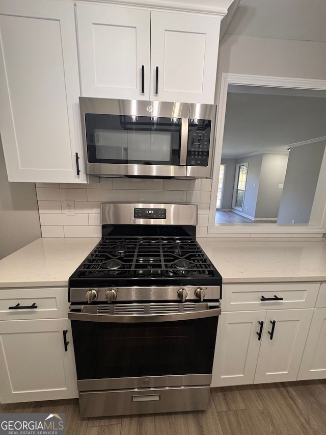 kitchen with dark wood-type flooring, appliances with stainless steel finishes, backsplash, light stone countertops, and white cabinets