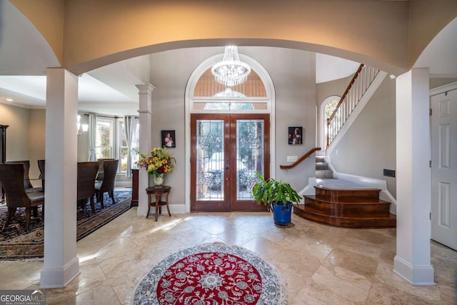 foyer entrance with decorative columns, a chandelier, a high ceiling, and french doors