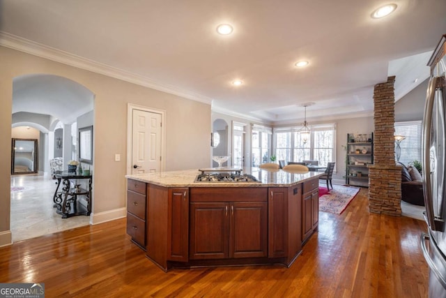 kitchen with stainless steel gas stovetop, hanging light fixtures, dark wood-type flooring, a center island, and decorative columns