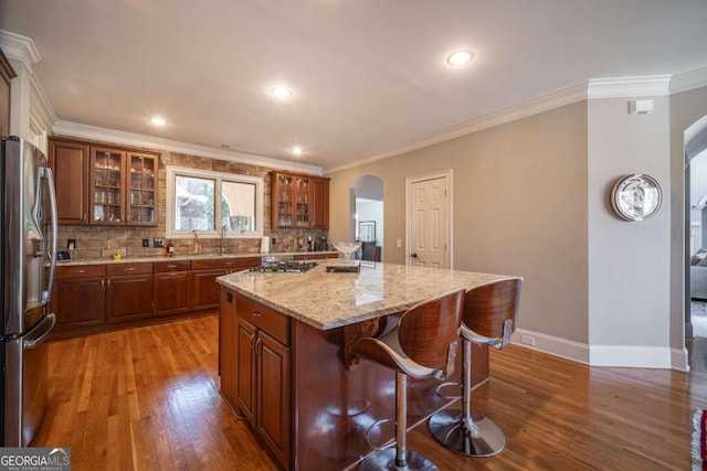 kitchen featuring appliances with stainless steel finishes, a kitchen island, dark wood-type flooring, light stone counters, and crown molding