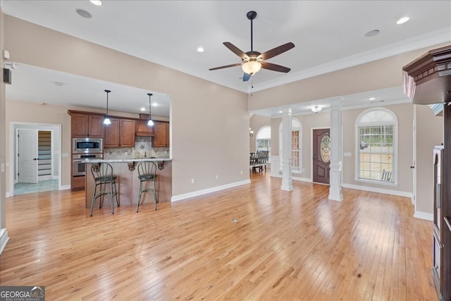 living room featuring decorative columns, light hardwood / wood-style floors, crown molding, and ceiling fan