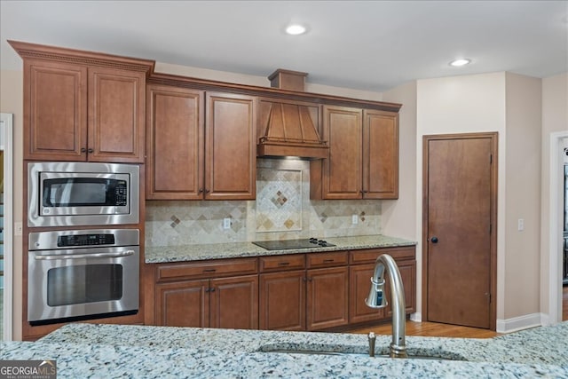 kitchen featuring light stone countertops, appliances with stainless steel finishes, custom exhaust hood, decorative backsplash, and sink