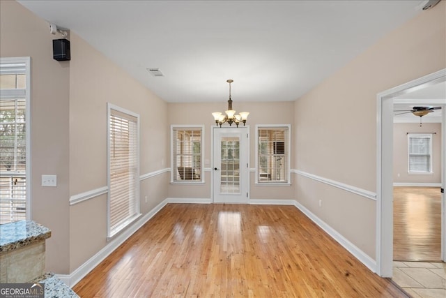 unfurnished dining area with ceiling fan with notable chandelier and light hardwood / wood-style flooring