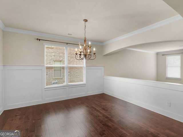 unfurnished dining area with ornamental molding, dark wood-type flooring, wainscoting, and a notable chandelier