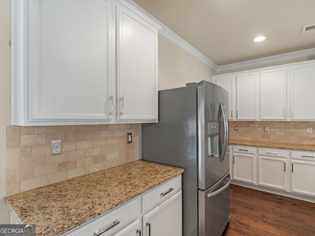 kitchen featuring light stone counters, ornamental molding, stainless steel fridge, and white cabinetry