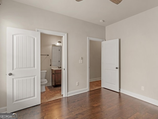 unfurnished bedroom with ensuite bathroom, dark wood finished floors, and baseboards