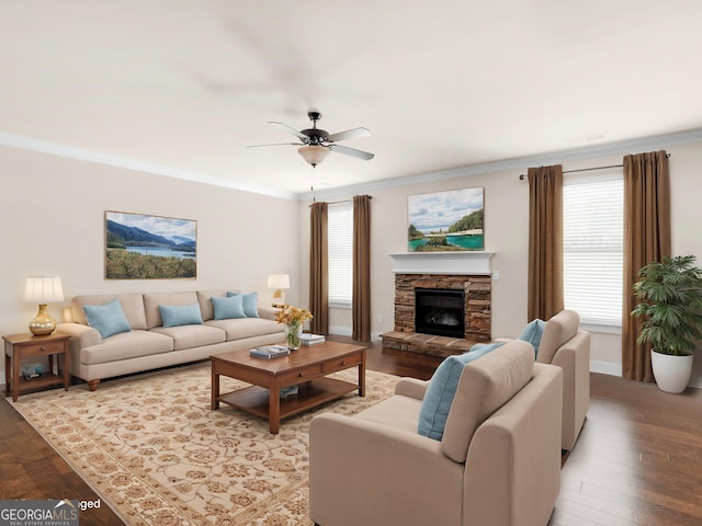 living room featuring a ceiling fan, light wood-type flooring, crown molding, and a stone fireplace