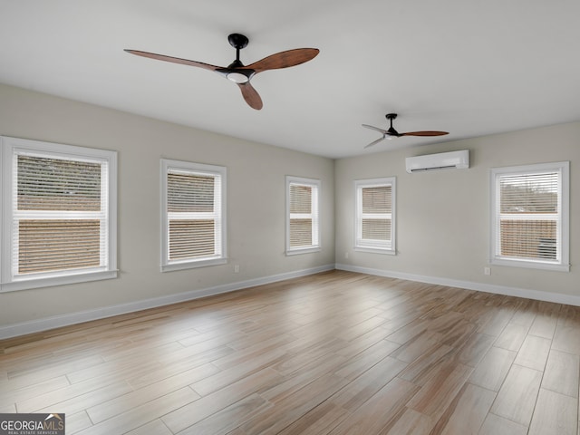 empty room with ceiling fan, a wall mounted AC, light wood-type flooring, and baseboards