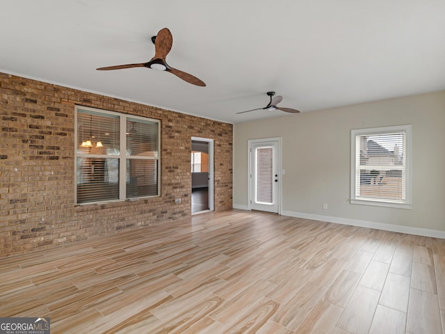 unfurnished living room with ceiling fan, brick wall, light wood-style flooring, and baseboards