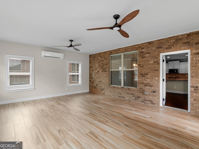 interior space featuring ceiling fan, light wood-style flooring, brick wall, baseboards, and a wall mounted AC