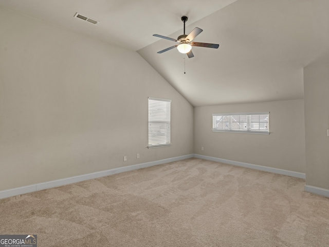 empty room with lofted ceiling, light colored carpet, visible vents, and baseboards