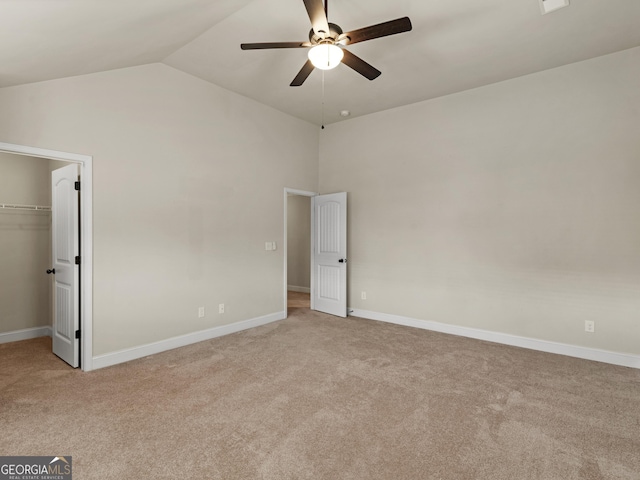 unfurnished bedroom with light carpet, vaulted ceiling, a spacious closet, and baseboards