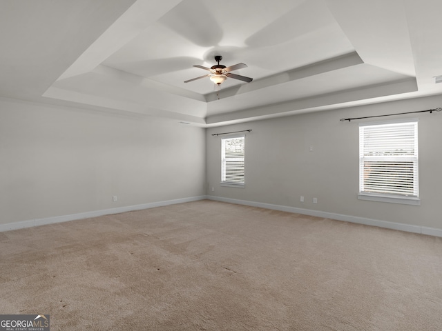 empty room featuring a ceiling fan, a raised ceiling, light colored carpet, and baseboards