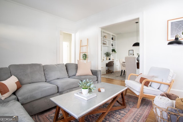 living room with crown molding, built in shelves, and wood-type flooring