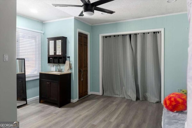 interior space featuring a textured ceiling, sink, ornamental molding, ceiling fan, and light hardwood / wood-style flooring