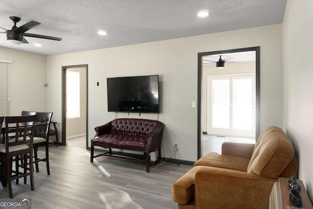 living room featuring light hardwood / wood-style floors, a textured ceiling, and ceiling fan