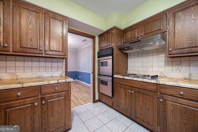 kitchen featuring light tile patterned flooring, light stone counters, ornamental molding, stainless steel appliances, and backsplash