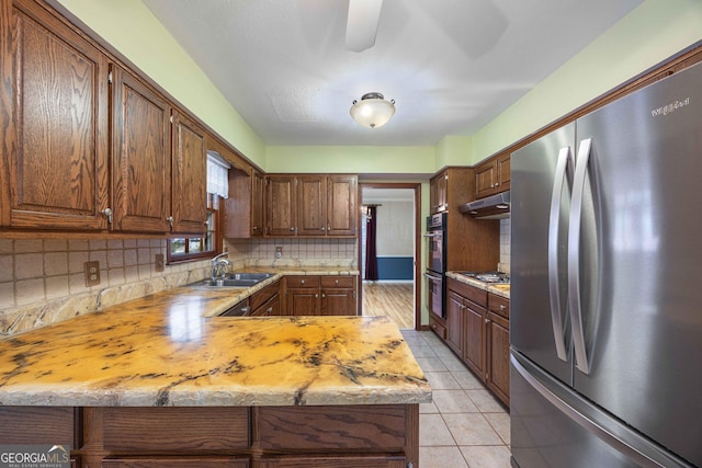 kitchen featuring sink, light tile patterned floors, appliances with stainless steel finishes, kitchen peninsula, and backsplash