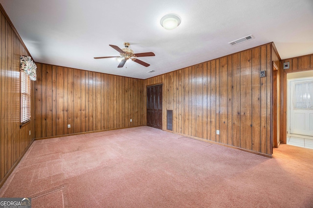 carpeted empty room with ceiling fan, a healthy amount of sunlight, and wood walls