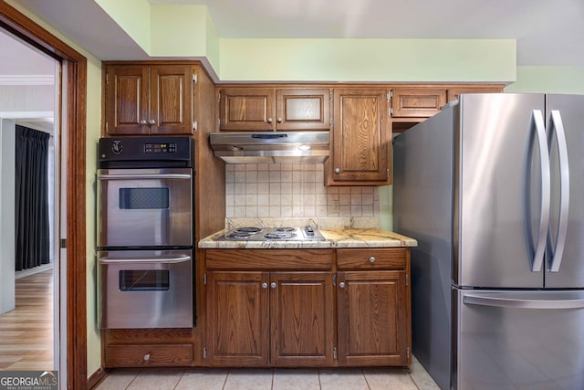 kitchen with light tile patterned flooring, light stone counters, crown molding, appliances with stainless steel finishes, and backsplash