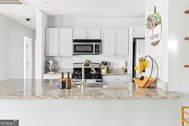 kitchen with appliances with stainless steel finishes, sink, white cabinets, and light stone counters