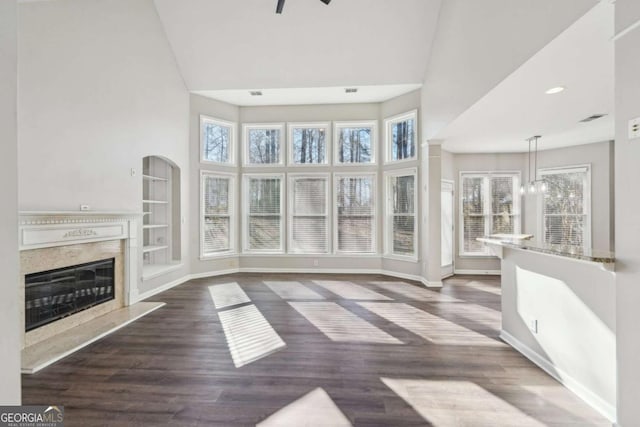 unfurnished living room with ceiling fan, dark wood-type flooring, a high ceiling, and a high end fireplace