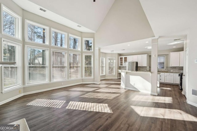 unfurnished living room with dark hardwood / wood-style floors, high vaulted ceiling, and ornate columns