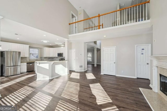 unfurnished living room with a towering ceiling, a high end fireplace, ornate columns, and dark wood-type flooring